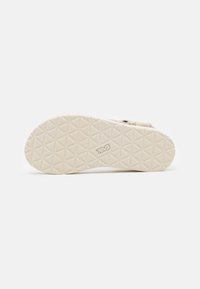 Light beige rubber sandal sole with a geometric tread pattern and embossed logo. Textured surface provides grip and durability.