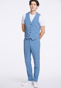 Ljusblå väst och matchande byxor tillverkade av ett mjukt tyg, med en femknapplåsning och två framfickor. Kombinerat med vita skor.