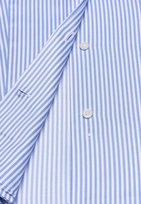 Tessuto di camicia a righe azzurro chiaro e bianco, con chiusura a bottoni e un'apertura piccola. Texture liscia con linee orizzontali.