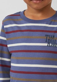 Kind dat een blauw, wit, bruin en rood gestreepte trui draagt met de tekst "TEAM ROAR" op de borst, weergegeven van de nek tot het midden van de torso.