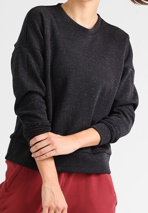 Person wearing a dark gray speckled long-sleeve sweatshirt and red pants, with one hand holding the opposite forearm.