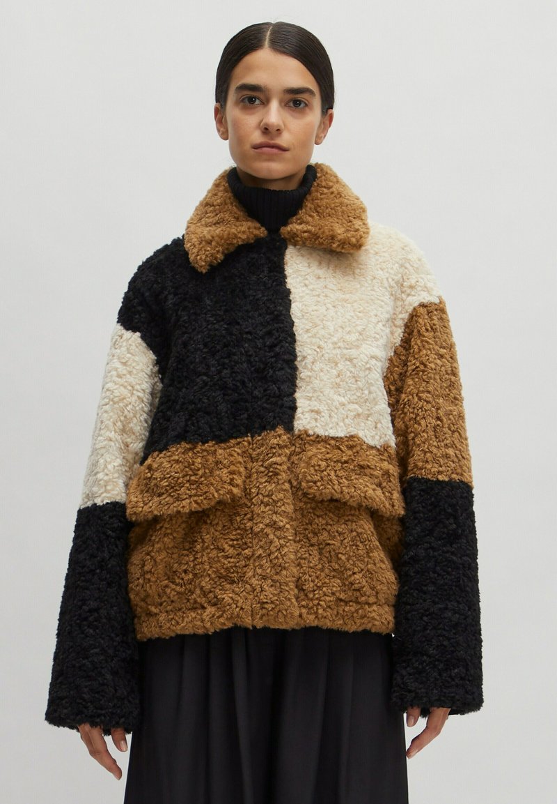 Fleecejacke mit einem Patchwork-Design in Braun, Schwarz, Creme und Tan. Sie hat einen Kragen und übergroße Ärmel.