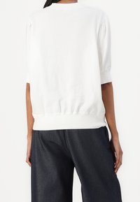 Vit kortärmad topp med samlad nederkant och rund halsringning; mjukt bomullsmaterial. Matcher med lösa mörka denimbyxor.