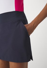 Mörkblå sportskort med bred midjeresår, sidficka och slits vid fållen. Tillverkad i ett mjukt, lätt tyg.