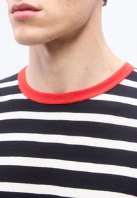 Κοντινό πλάνο του κάτω μέρους του προσώπου και του λαιμού ενός ατόμου που φοράει πουκάμισο με μαύρες και άσπρες ρίγες και κόκκινο γιακά.