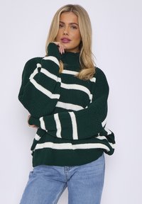 Green striped sweater with white horizontal stripes, ribbed texture, high neck, and relaxed fit, paired with blue jeans.