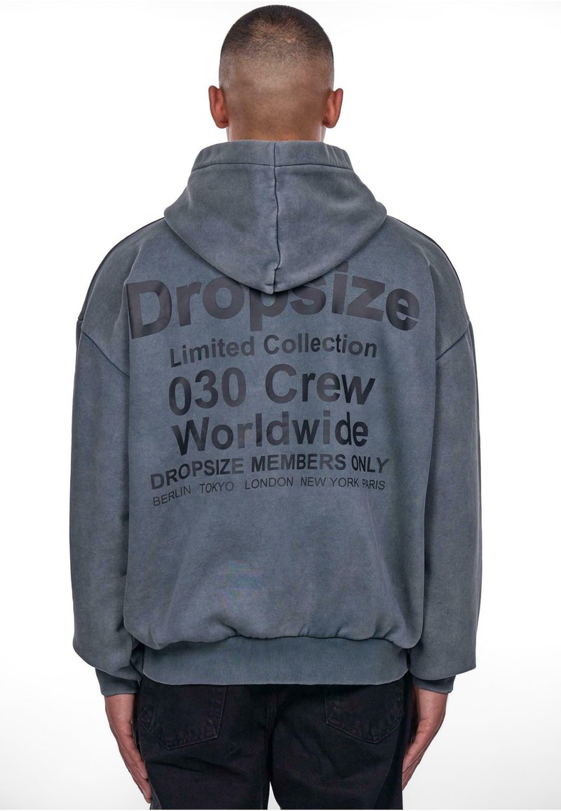 Kapuzensweatshirt in gedecktem Grau mit auffälligem schwarzen Text auf der Rückseite. Design mit fallenden Schultern und gerippten Bündchen und Saum.