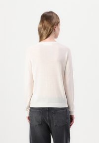 Lys rosa, lett strikket genser med lange ermer og rund hals. Jevn tekstur, ribbestrikket kant og detaljer i baksemen.