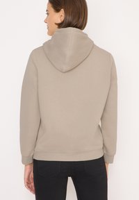 Světle béžová mikina s kapucí na šňůrku, žebrovanými manžetami a lemem. Měkká textura a minimalistický design. Nosit s černými džíny.