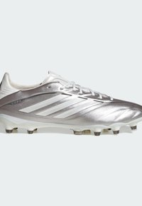 Chaussure de soccer Adidas Copa argentée avec trois bandes blanches, lacets et crampons moulés sur un fond clair.