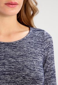 Navyblaue strukturierte Bluse mit rundem Ausschnitt. Der Stoff zeigt ein meliertes Muster und enthält Akzente in helleren Farbtönen für visuelles Interesse.