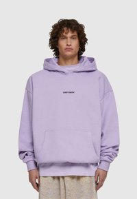 Violeta kokvilnas kapuce ar priekšējo kabatu, pārmērīga izmēra, un izšūts "LOST YOUTH" logo melnā krāsā centrā uz krūšu.