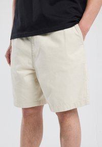 Pantalones cortos de color beige claro, confeccionados en algodón, con una cinturilla elástica, bolsillos laterales y un corte relajado. El dobladillo está terminado con una costura cuidada.