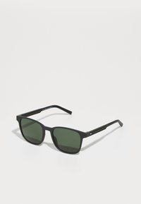 Ochelari de soare rectangulare negri cu lentile verzi închise, având un finisaj mat și brațe texturate. Include un accent mic cu logo-ul brandului pe lateral.