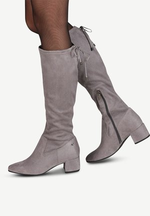 Szare zamszowe kozaki sięgające do kolan z grubym obcasem, suwakiem z boku i sznurkiem u góry, noszone z przezroczystymi czarnymi rajstopami.