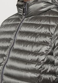 Šedá péřová bunda s prošívanými sekcemi, vysokým límcem a předním zipem se tmavým kovovým kováním. Hladký, lesklý textilní povrch.