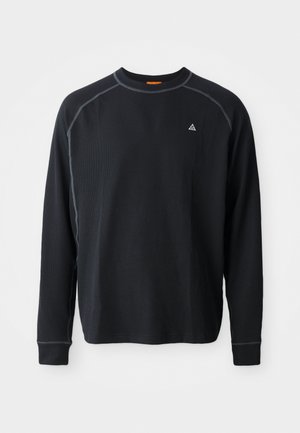 Chemise noire à manches longues en tissu texturé. Dispose d'un col rond, de coutures contrastées, et d'un petit logo sur la poitrine. Coupe regular.