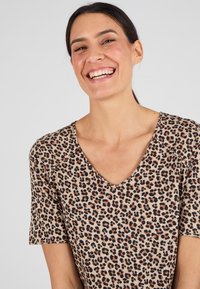 Leopardprint V-hals t-shirt met korte mouwen, zachte stof, beige achtergrond met zwarte en bruine vlekken, ontspannen pasvorm.