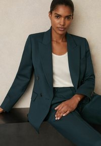 Tirkīza divrindas blazera ar struktūrētām plecu daļām, apvienots ar vieglu t-kreklu. Gluda auduma, piegriezuma fit un minimālistiskās dizaina detaļas.