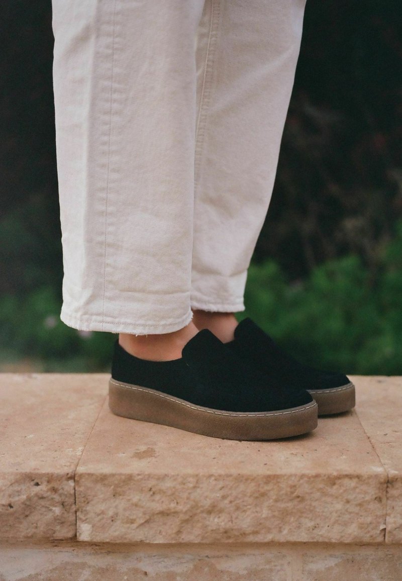 Juodos suėtos slip-on tipo bateliai su apvaliu batu, su šviesiai rudu guminiu padu. Sukomplektuoti su baltais trumpais džinsais.