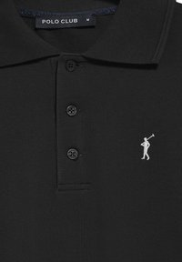 Svart polotröja med texturerat tyg, tre svarta knappar och en liten vit broderad golffigur på vänster bröst.