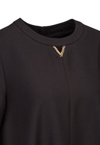 Schwarzes Oberteil mit Rundhalsausschnitt, strukturiertem Stoff und einem goldenen Kettenakzent in V-Form am Ausschnitt. Glatte Textur, minimalistisches Design.