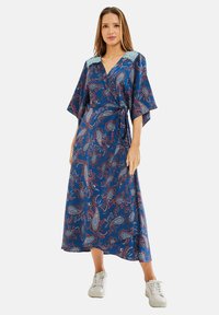 Long blue dress with paisley pattern in red and white. Features a v-neck, loose sleeves, and a tie waist. Lace accents on shoulders.
