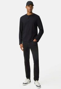 Zwarte langelijno ver uit henley shirt met een drie-knopen placket, gecombineerd met zwarte jeans en witte sneakers. Eenvoudig, casual ontwerp met een getailleerde silhoeet.