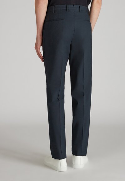 Pantalones marinos con un corte ajustado, textura suave y dos bolsillos traseros, combinados con zapatillas blancas.