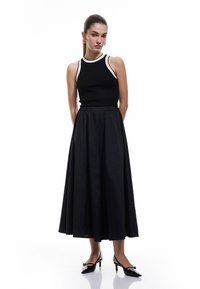 Top negro acanalado con ribete blanco, combinado con una falda negra fluida. El modelo lleva unos tacones negros de punta con detalles decorativos.