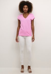 Roze V-hals t-shirt met korte mouwen, gemaakt van katoen, gecombineerd met witte skinny jeans en naaktkleurige blokhaksandalen. Eenvoudig ontwerp, casual uitstraling.