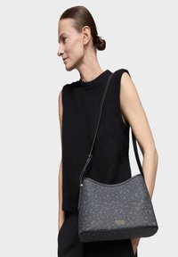 Bolso estructurado negro hecho de material texturizado con un patrón sutil, que presenta una correa larga y un acento de logo dorado.