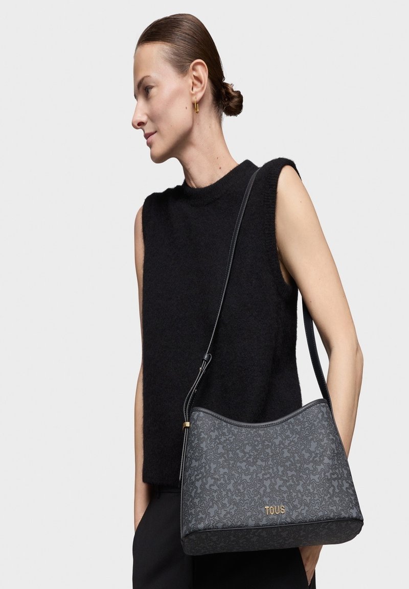 Bolso estructurado negro hecho de material texturizado con un patrón sutil, que presenta una correa larga y un acento de logo dorado.