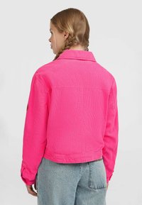 Roze corduroy jasje met verlaagde schouders, knoopmanchetten en een cropped fit, met een ronde patch op de linker mouw.