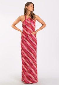 Vestido maxi con un diseño asimétrico, que presenta una tela estampada en tonos rosa y rojo, tirantes finos y un detalle recortado en la cintura.