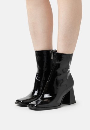 Black patent leather ankle boots with a square toe, chunky heel, and side zipper, featuring a glossy finish and sleek design.