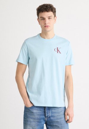 Light blue short-sleeve t-shirt in cotton fabric with a round neckline, featuring a dark maroon "ck" logo on the left chest area.
