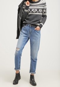 Neulepaita, jossa tummanharmaa ja valkoinen sydänkuvio, yhdistetty vaalean sinisiin repaleisiin farkkuihin. Mustat nilkkurit täydentävät asun.