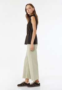 Mustaton hihaton toppi, jossa on kireä muotoilu, yhdistettynä vaaleanvihreisiin leveälahkeisiin farkkuihin, joissa on raikkaat helmat. Jalkineet ovat tummanruskeat tennarit.