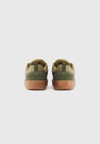 Et par olivengrønne Puma sneakers med gummisåler vist fra bagsiden på en ensfarvet hvid baggrund.