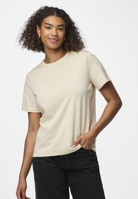 En kortermet kremfarget t-skjorte laget av mykt stoff, med en klassisk rund hals og en avslappet passform, sammen med mørke jeans.