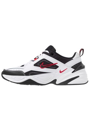 Baskets Nike blanches, noires et rouges avec une tige en mesh et cuir, semelle épaisse, logos swoosh rouges et languette arrière.
