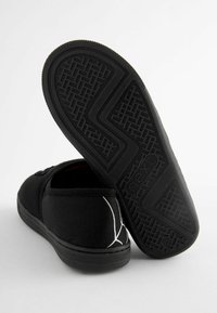 Scarpe slip-on in tessuto nero con suola in gomma testurizzata. Caratteristiche includono cuciture bianche a contrasto e un design semplice per un facile utilizzo.
