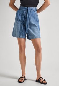 Denimshorts med bälte i midjan, i ljusblå färg, lös passform, veck och uppvikta fållar. Kombineras med svarta sandaler med remmar.