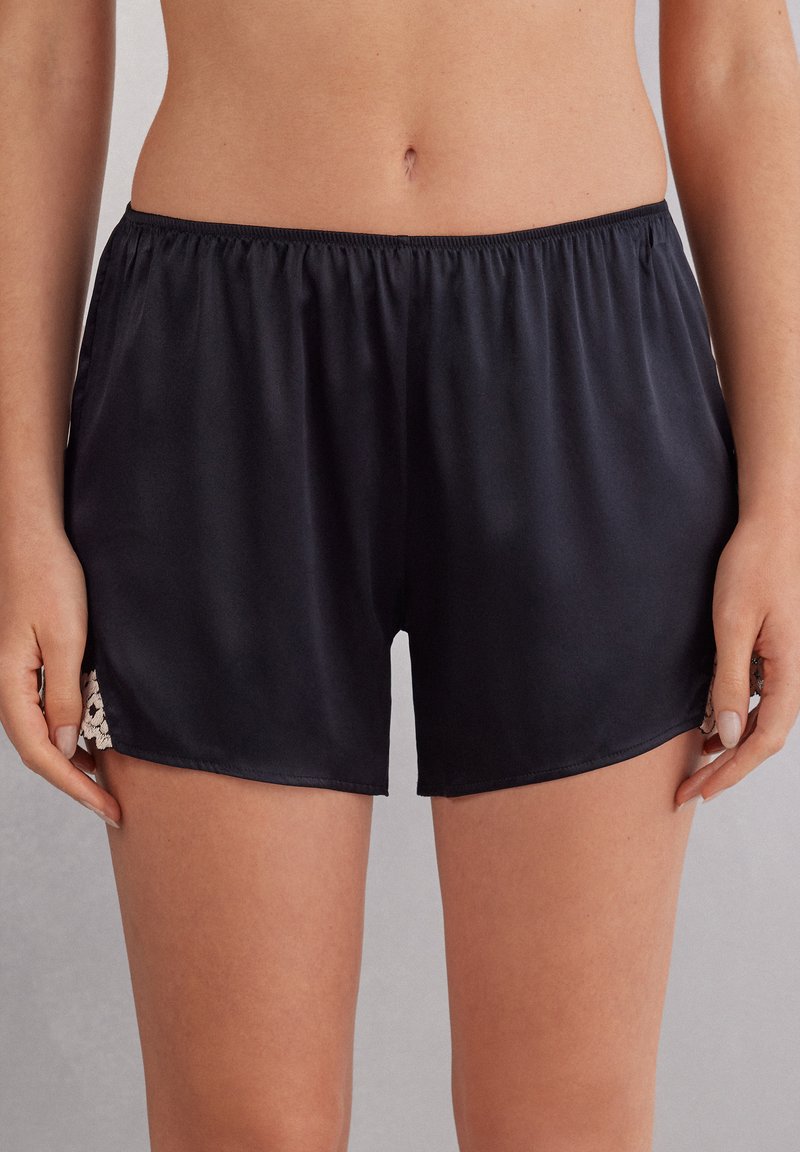 Zwarte satijnen shorts met een elastische tailleband, voorzien van kantaccenten aan de zijkanten en een gladde, glanzende textuur.