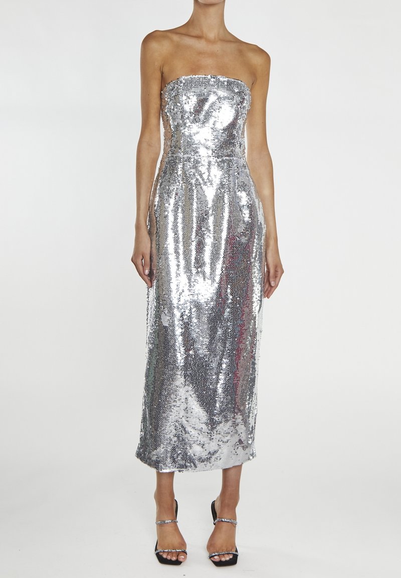 Robe de soirée sans bretelles, ornée de sequins argentés, silhouette ajustée, longueur genoux, texture lisse, coutures plates, portée avec des sandales noires à talons.