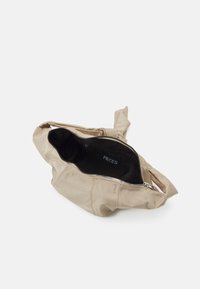 Beige axelväska med mjukt yttermaterial, dragkedjestängning och en knuten handtag. Den svarta innerväggens foder har en varumärkesetikett.