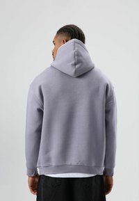 Hoodie in lichtlavendel, voorzien van een zachte stof, een losse pasvorm en geribbelde manchetten. Achteraanzicht toont de capuchon en stiksel details.