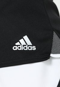 Černá sportovní tkanina s bílým logem "adidas", vyznačující se texturovaným designem a kontrastními bílými a vzorovanými akcenty na lemu.