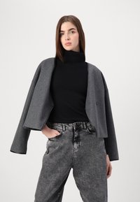 Γκρι κοντό μπουφάν από μείγμα μαλλιού, με φαρδιές μανσέτες και κλείσιμο με έναν μόνο κουμπί, φορεμένο πάνω από μαύρο ζιβάγκο και γκρι τζιν.